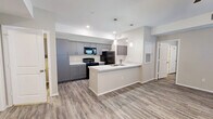 This single-story 2-bedroom, 2-bathroom unit offers a thoughtfully designed open-concept layout connecting the kitchen and living area. The kitchen is outfitted with sleek gray cabinetry, quartz-style countertops, black appliances including a range, microwave, and refrigerator, and a peninsula with a built-in sink — ideal for both meal prep and casual dining. Stylish pendant lighting accents the space, and wood-look flooring runs consistently throughout the entire unit, lending a cohesive and modern aesthetic.

The living area is generously sized, featuring a ceiling fan, neutral-toned walls, and natural light from blinds-covered windows. Both bedrooms are well-proportioned, bright, and share the same warm, neutral palette and durable flooring. The primary bedroom includes its own closet with built-in shelving and hanging rods for ample storage.

Each bathroom features a gray vanity with white countertop, a walk-in shower, and overhead lighting with a large mirror. The dedicated laundry room includes overhead gray cabinetry matching the kitchen, washer and dryer hookups, and a utility sink connection. A separate utility room and additional closets round out the functional layout of this clean, move-in-ready space.
