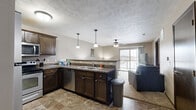 Located at 4600 E 54th St in Sioux Falls, SD, this well-appointed one-bedroom, one-bathroom unit offers a thoughtfully designed open floor plan that maximizes every square foot. The kitchen and living area flow seamlessly together, creating a comfortable and functional shared space. The kitchen is outfitted with dark espresso cabinetry, granite-style countertops, stainless steel appliances including a refrigerator, range, and microwave, and a double-basin sink. A peninsula with bar seating and pendant lighting above adds both style and practicality. Tile flooring runs throughout the kitchen and connects naturally to the carpeted living room, which features a ceiling fan and a sliding glass door that opens to a private balcony with open outdoor views. The bedroom is a calm, carpeted retreat with a large window that invites natural light and provides ample space for a full furniture arrangement. The bathroom features tile flooring, a dark vanity with granite-style counters, and a shower-tub combination. A dedicated closet and in-unit washer hookup add convenience. Textured ceilings and neutral warm-gray walls give the space a cohesive, move-in-ready aesthetic throughout.