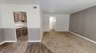 This single-floor residence offers a well-organized layout designed for comfortable, everyday living. The living area serves as the heart of the home, featuring a combination of durable wood-look vinyl flooring and soft carpeting, a textured ceiling, and a ceiling fan overhead. Two-tone walls with a gray lower accent add a modern touch, while large sliding glass doors with vertical blinds invite abundant natural light and provide access to an outdoor balcony with green views beyond. The galley-style kitchen is efficiently arranged with dark wood cabinetry lining both walls, light quartz-style countertops, a stainless steel sink, and white appliances including a refrigerator, dishwasher, and electric range — all set atop matching wood-look flooring. The bedrooms are carpeted for warmth and comfort; one features a distinctive painted brick accent wall, track lighting, and a sliding-door closet, while the other is spacious with neutral gray walls and a large window. The bathroom is clean and functional, with a single-sink vanity, a toilet, and a full tub-shower combo finished with classic white tile. Throughout, the space maintains a cohesive, neutral palette that is both practical and inviting.
