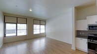 This single-floor space offers a clean, minimalist aesthetic defined by its light hardwood flooring and crisp white walls. The main living area is open and airy, benefiting from multiple windows fitted with sleek black-framed roller shades that allow for adjustable natural light throughout the day. The smooth, light-toned flooring reflects incoming daylight, enhancing the sense of openness within the room. Recessed ceiling lighting provides additional illumination, complementing the natural light and ensuring the space remains bright at all hours. The neutral color palette of the walls and flooring creates a versatile backdrop well-suited for a variety of interior styles and furnishing choices. White baseboards provide a clean border between the walls and flooring, contributing to the space's polished, contemporary feel. The layout appears straightforward and functional, with open wall space offering flexibility for furniture arrangement. Overall, the space presents a modern, well-lit environment with a calm and understated ambiance.