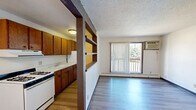 This one-bedroom, one-bathroom unit in Rapid City, South Dakota, offers an efficiently designed single-floor layout with a functional open-concept arrangement. The kitchen and living area flow together, separated by a distinctive structural column with built-in open shelving, adding character and practical storage. The kitchen features warm wood-toned cabinetry, white countertops, a gas range, a double sink, and a full-size refrigerator, providing all essential cooking amenities.

The living area is bright and open, with light hardwood-style flooring extending throughout. A sliding glass door fitted with vertical blinds leads to a private balcony, allowing natural light to fill the space and providing outdoor views of surrounding greenery. A wall-mounted air conditioning unit and baseboard heating ensure year-round comfort.

The bedroom is a comfortable size, featuring a sliding-door closet, a window with natural light, and the same hardwood-style flooring. The full bathroom includes a tub-shower combination with built-in shelving, a vanity with a wood-framed mirror, and clean, neutral finishes. A textured ceiling is consistent throughout the unit. Residents also have access to an outdoor pool area surrounded by mature trees.