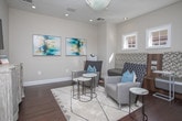Located at 1717 Lavista Rd NE in Atlanta, Georgia, this thoughtfully designed single-floor space combines contemporary style with functional comfort. Rich, dark hardwood flooring runs throughout, providing a warm and elegant foundation that complements the neutral, soft-gray walls.

The main lounge area is a welcoming focal point, anchored by a statement chandelier with an organic, sculptural form that draws the eye upward. A wall-mounted flat-screen television sits above a decorative carved sideboard, while a curated seating arrangement — including gray upholstered chairs and marble-topped accent tables — creates an inviting atmosphere. Two vibrant abstract art pieces add a splash of color against the clean walls.

A built-in seating nook with a textured herringbone-upholstered bench offers a comfortable secondary gathering spot, complemented by natural light streaming through multiple windows. The nook also accommodates a workspace area, making the space as practical as it is stylish.

Large gridded windows and a full-length glass door open directly to an outdoor patio and pool area, framing lush seasonal foliage and bringing the outdoors in. The seamless indoor-outdoor connection is a standout feature, ideal for relaxed gatherings or a quiet retreat. Recessed lighting throughout ensures the space is well-illuminated at all times.