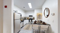 This single-floor residence offers a thoughtfully designed layout with a clean, modern aesthetic carried throughout each space. The kitchen serves as a functional centerpiece, featuring white cabinetry, dark granite countertops, stainless steel appliances including a refrigerator, range, and dishwasher, and wood-look vinyl flooring. A dining counter with seating for two provides a convenient casual dining option, and an in-unit laundry area is conveniently accessible directly from the kitchen.

The living area accommodates comfortable seating and benefits from natural light through large windows dressed with floor-length curtains. The bedrooms maintain the same neutral, modern palette, with wood-look flooring and ample natural light. A standout feature in one of the bedrooms is a built-in floating desk and shelving nook with under-cabinet lighting, ideal for a dedicated workspace. A full-length mirror and access to a closet further enhance the room's functionality.

The bathrooms are finished with white cabinetry, dark granite countertops, and wood-look flooring. Each features a tub-shower combination and clean white walls, maintaining a bright, cohesive feel consistent with the rest of the residence.