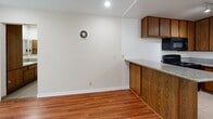 This single-floor space is designed with a practical and cohesive layout that connects its main living areas seamlessly. The living and dining areas are finished with warm-toned hardwood flooring that extends throughout much of the unit, creating a consistent and inviting aesthetic. Recessed lighting and a ceiling fan overhead provide both illumination and ventilation, while a wall-mounted ventilation unit in the living area offers additional climate control. Natural light filters in through a window dressed with vertical blinds, brightening the open space.

The kitchen is positioned adjacent to the living area and separated by a peninsula counter finished with granite-style countertops and warm oak cabinetry. The kitchen itself is fully equipped with black appliances, including a gas range, over-the-range microwave, and a double-basin sink. Light tile flooring in the kitchen contrasts with the hardwood in the living areas. Ample upper and lower cabinetry provides generous storage throughout.

The bedrooms continue the hardwood flooring and feature mirrored sliding closet doors that enhance the sense of space and light within each room. The bathroom includes a granite-topped vanity with oak cabinetry, a wall-mounted mirror cabinet, and a tub-shower combination enclosed by sliding glass doors, all finished with neutral tile flooring.