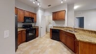 This single-floor residence offers a thoughtfully designed layout with consistent finishes throughout. The kitchen is a functional centerpiece, featuring warm wood cabinetry, granite countertops, and a full suite of black appliances including a range, microwave, and dishwasher. A curved peninsula with a stainless steel sink opens directly into the living area, creating a seamless flow for everyday living and entertaining. The living room is generously sized, with plush carpeting, a ceiling fan, and a sliding glass door fitted with vertical blinds that offers views of lush greenery outside. Adjacent carpeted bedrooms provide comfortable retreats; the primary bedroom benefits from a curved bay window arrangement that invites natural light and features its own ceiling fan. The primary bathroom is well-appointed with a double-sink granite vanity, rich wood cabinetry, tile flooring, and a glass-enclosed shower. A second bathroom mirrors the same granite and wood aesthetic with a single vanity. A dedicated in-unit laundry room with side-by-side washer and dryer adds practical convenience. The entry foyer greets residents with a paneled white door and tile flooring, establishing a clean and welcoming first impression throughout this well-maintained home.