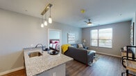 This thoughtfully designed single-floor residence offers a seamless open-concept layout connecting the kitchen, dining, and living areas. The kitchen is outfitted with stainless steel appliances, including a refrigerator, range, and built-in microwave, complemented by warm wood-toned cabinetry, granite countertops, and a peninsula with an undermount sink and pendant lighting overhead. The living area features wood-style flooring, a ceiling fan, and windows that allow natural light to fill the space.

Two well-appointed bedrooms provide comfortable retreats, each with wood-style flooring, ceiling fans, and windows offering outdoor views. The primary bedroom benefits from abundant natural light through multiple windows, while the second bedroom carries a cozy, relaxed character.

The unit includes two bathrooms: one featuring a glass-enclosed walk-in shower and granite vanity, and the other offering a shower-tub combination with a decorative curtain and matching granite countertop. A spacious walk-in closet with wire shelving and hanging rods provides ample storage. Neutral gray wall tones throughout create a clean, cohesive aesthetic that complements the modern finishes found across the entire residence.