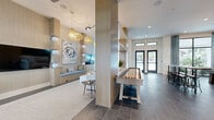 Located at 100 Boucle Jeanne Circle in Maitland, Florida, this thoughtfully designed single-floor community space offers a seamless blend of contemporary style and coastal elegance. The open-concept layout connects a spacious living area with a formal dining room, creating a cohesive and inviting environment throughout.

The living area is anchored by an elongated lounge space featuring light wood built-ins, a cushioned bench seat with aqua blue accents, and an eye-catching oversized floral artwork. Woven rattan pendant lights hang at varying heights, adding warmth and texture to the airy, neutral palette. Floor-to-ceiling windows and sliding glass doors flood the space with natural light while offering direct views of the outdoor pool area, creating a seamless indoor-outdoor connection.

The dining room is a standout feature, distinguished by striking blue-toned abstract wallcovering that spans the full height of the wall, exposed wood beam cathedral ceilings, and a herringbone-patterned tile floor. A large communal wood dining table surrounded by upholstered chairs sits beneath modern drum pendant lights, making the room ideal for gatherings.

Large-format slate tile flooring runs throughout the space, tying the rooms together cohesively. The overall ambiance is bright, sophisticated, and resort-inspired, reflecting a carefully curated Florida coastal aesthetic.