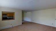 Located at 134 Innis Ave in Poughkeepsie, New York, this single-floor residence offers a straightforward and functional layout designed for comfortable everyday living. The interior is finished with neutral, light-toned walls that create a clean and airy atmosphere throughout the space. The main living area is generously sized, featuring wall-to-wall carpeting in warm, understated tones that add a sense of coziness to the room. A ceiling fan is positioned toward the rear of the living space, providing both air circulation and a subtle decorative element. The open layout of the living area allows for flexible furniture arrangement, making it adaptable to a variety of living styles. A pass-through window connects the living area to the kitchen, which features wood-toned cabinetry visible from the main room — a practical detail that enhances the flow between spaces. The clean white ceiling and simple trim work throughout maintain a cohesive, uncluttered aesthetic. The overall ambiance is calm and neutral, offering a blank canvas well-suited for personalization. Situated in Poughkeepsie, the property benefits from its Hudson Valley location, with access to local amenities, parks, and transportation options.