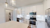 This thoughtfully designed one-bedroom, one-bathroom unit offers a clean, modern aesthetic across a single floor. The open-concept kitchen and living area serves as the heart of the home, showcasing white shaker cabinetry, a white subway tile backsplash, quartz countertops, and a full suite of stainless steel appliances including a side-by-side refrigerator with water dispenser, electric range, built-in microwave, and dishwasher. A large center island provides additional prep and dining space, while glass pendant lighting adds a contemporary finishing touch. Warm wood-style flooring runs throughout the entire unit, creating a cohesive and inviting atmosphere. The bedroom is a comfortable, well-lit retreat featuring a ceiling fan, multiple windows with blinds for natural light and privacy, and a sliding glass door that opens to an outdoor view of greenery. The bathroom is finished with white cabinetry, quartz countertops, and clean, bright surfaces. An in-unit washer and dryer is also included. Neutral wall tones and abundant natural light give the space a fresh, airy feel throughout.