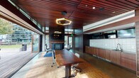 Located at 2135 6th Ave in Seattle's Belltown neighborhood, this single-floor amenity space combines contemporary design with warm, natural materials to create a refined and functional environment. The space is unified by rich wood-slatted ceilings that run throughout, lending a cohesive, upscale character to every area.

The main lounge centers around a striking concrete fireplace topped with a live-edge wood mantel and a mounted flat-screen television, flanked by speakers for an immersive audio-visual experience. Comfortable lounge seating surrounds the fireplace, creating an inviting gathering area. Adjacent to the lounge, a live-edge wood conference table with ergonomic chairs provides a polished setting for meetings or collaborative work, illuminated by a geometric pendant light fixture.

A wet bar area along one wall features custom wood cabinetry, a sink, and a white tile backsplash with frosted glass upper cabinets, ideal for hosting events. The space also includes a billiards area, accessible through dramatic dark-wood doors with frosted glass panels. Polished concrete and hardwood flooring transitions guide movement between zones. Large glass walls and doors open to an outdoor terrace, flooding the interior with natural light and offering views of the surrounding Seattle cityscape.
