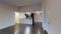 This single-floor residence offers a thoughtfully designed open-concept layout that promotes a sense of spaciousness and easy flow between living areas. Rich, dark hardwood flooring extends throughout, adding warmth and a polished finish underfoot.

The kitchen is a standout feature, showcasing dark espresso-toned cabinetry that reaches toward the ceiling for ample storage. Stainless steel appliances, including a microwave and range, are integrated seamlessly into the design. A peninsula with a light stone-toned countertop serves as both a functional workspace and a natural divider between the kitchen and the open living area, making it ideal for entertaining or casual dining.

The living area is generously proportioned, benefiting from the open sightlines that extend across the entire common space. A ceiling fan overhead provides both comfort and ambient lighting. Neutral-toned walls throughout create a clean, versatile backdrop that complements a variety of interior styles.

Natural light filters into the space, enhancing the airy feel of the interior. An entryway with a classic white door provides a welcoming arrival point, while additional doorways hint at private areas beyond the main living zone. Overall, the space combines modern finishes with practical design for comfortable everyday living.