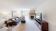 Located at 500 E Centennial Drive in Oak Creek, Wisconsin, this well-appointed two-bedroom, two-bathroom residence offers comfortable single-floor living with a thoughtful layout. The open-concept kitchen is a functional centerpiece, featuring rich cherry-toned cabinetry, black appliances including a refrigerator and range, a peninsula breakfast bar with seating, track lighting, and hardwood-style flooring. A window over a small built-in desk area brings in natural light and views of the surrounding greenery. The spacious living room is anchored by a tile-surround fireplace and features plush carpeting, large windows, and a sliding glass door that opens to the outdoors. The primary bedroom is generously sized with soft carpet, neutral tones, and a closet. The second bedroom is equally comfortable, also featuring carpet and a closet. Both bathrooms are finished with tile flooring, white cabinetry vanities, and clean, bright aesthetics. A dedicated laundry room adds everyday convenience. Outside, the brick exterior building is set against a beautifully landscaped community with a serene pond, manicured lawn, and mature trees—offering a peaceful and scenic outdoor setting.