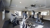 This fitness center offers a comprehensive workout environment housed in a single-level space with a clean, functional design. The room features tray ceilings with crown molding, adding a refined architectural touch that elevates the space beyond a typical gym setting. Two ceiling fans are installed to promote air circulation throughout, while recessed lighting provides consistent, even illumination across the floor.

The cardio section includes elliptical trainers and treadmills positioned near the windows, allowing natural light to filter in during workouts. A multi-station cable machine anchors the strength training area, complemented by a dedicated dumbbell rack with a full range of free weights. A weight bench and additional resistance equipment round out the strength training offerings. Rubber flooring is laid throughout, providing durable, impact-absorbing coverage suited for varied exercise activities.

Large mirrors are mounted along one wall, enhancing the sense of space and allowing users to monitor their form. The neutral color palette of warm beige walls and white trim creates a clean, focused atmosphere. Overall, the space is thoughtfully organized to accommodate both cardio and strength training in an accessible, well-maintained environment.
