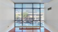 Located at 109 Church St in the heart of downtown New Haven, CT, this single-floor unit offers a thoughtfully designed layout that balances open living spaces with functional private areas. The standout feature is the expansive floor-to-ceiling window wall fitted with adjustable horizontal blinds, flooding the main living area with abundant natural light while framing dynamic views of the bustling Church Street corridor, including tree-lined sidewalks and neighboring urban architecture. Rich, warm-toned hardwood flooring extends throughout the living and bedroom spaces, lending a sense of continuity and elegance across the unit. The open living area is generously proportioned, offering flexible arrangement potential, while a separate bedroom provides a quieter retreat with its own large street-facing windows. The kitchen is efficiently appointed with a full electric range, over-the-range microwave, and ample cabinetry. The bathroom features a full tub-shower combination with tile surround, a vanity with granite countertop, and clean tile flooring. The unit's modern architectural design, combined with its prime New Haven location near Yale University and downtown amenities, makes it a compelling and practical urban space.