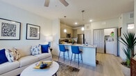 This well-designed single-floor residence offers a seamless blend of comfort and modern style. The open-concept layout connects the living room and kitchen, creating an inviting and functional space. The living area features light wood-style flooring, a ceiling fan, large windows that allow abundant natural light, and tasteful décor including framed artwork and a neutral sofa accented with bold blue throw pillows.

The kitchen is thoughtfully equipped with gray shaker-style cabinetry, granite countertops, a white subway tile backsplash, and stainless steel appliances including a refrigerator, electric range, and over-the-range microwave. A peninsula with a granite countertop and seating for three features pendant lighting overhead, making it ideal for casual dining or entertaining.

The bedroom is a serene retreat with large windows dressed in elegant drape panels, a ceiling fan, and ample space for a full dresser and bedside furnishings. The bathroom includes a soaking tub and shower combination with gray tile surround. A dedicated in-unit laundry area provides added convenience. Light wood-style flooring flows consistently throughout, unifying the space with a clean, contemporary aesthetic.
