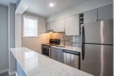 Located at 205 34th St. in Virginia Beach, VA, this single-floor unit offers a clean, modern aesthetic throughout. The open-concept living area is finished with light-toned luxury vinyl plank flooring and recessed lighting, creating a bright and welcoming atmosphere. Neutral gray walls are complemented by a striking blue accent wall that frames the pass-through kitchen window, serving as a stylish focal point between the living space and kitchen.

The kitchen is well-appointed with gray shaker-style cabinetry, marble-look quartz countertops, a stainless steel single-basin sink with a brushed nickel faucet, a stainless steel refrigerator, and a black electric range. A horizontal mosaic glass tile backsplash adds a contemporary touch, while a range hood provides practical ventilation.

The bedroom features the same durable wood-look flooring, soft gray walls, and dual windows that allow ample natural light to fill the room. A ceiling light fixture and closet space round out the room's functionality.

The bathroom is finished with large-format marble-look porcelain tile on both the floors and walls, lending an elegant, spa-like feel. It includes a dark-vanity with an integrated sink, a wall mirror with overhead lighting, and a window with plantation shutters for privacy and natural light.