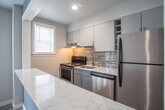 Located at 205 34th St. in Virginia Beach, VA, this single-floor unit offers a clean, modern aesthetic throughout. The open-concept living area is finished with light-toned luxury vinyl plank flooring and recessed lighting, creating a bright and welcoming atmosphere. Neutral gray walls are complemented by a striking blue accent wall that frames the pass-through kitchen window, serving as a stylish focal point between the living space and kitchen.

The kitchen is well-appointed with gray shaker-style cabinetry, marble-look quartz countertops, a stainless steel single-basin sink with a brushed nickel faucet, a stainless steel refrigerator, and a black electric range. A horizontal mosaic glass tile backsplash adds a contemporary touch, while a range hood provides practical ventilation.

The bedroom features the same durable wood-look flooring, soft gray walls, and dual windows that allow ample natural light to fill the room. A ceiling light fixture and closet space round out the room's functionality.

The bathroom is finished with large-format marble-look porcelain tile on both the floors and walls, lending an elegant, spa-like feel. It includes a dark-vanity with an integrated sink, a wall mirror with overhead lighting, and a window with plantation shutters for privacy and natural light.