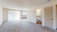 This single-floor unit offers a practical and well-organized layout across a series of interconnected rooms. The living area is spacious and filled with natural light, courtesy of large sliding glass doors that open to a private patio, complemented by vertical blinds for adjustable privacy. Soft wall-to-wall carpeting runs throughout the main living and bedroom spaces, lending warmth underfoot, while the textured ceiling adds a classic finish overhead.

The galley-style kitchen is efficiently designed with white cabinetry lining both sides, providing generous storage and counter space. It features a double-basin sink, a coil-burner electric range, a refrigerator, and a dishwasher. Wood-look flooring and a ceiling fan with light fixture round out the kitchen's functional appeal. A window allows natural light to brighten the cooking space.

The bedrooms are generously sized, each with plush carpeting and ceiling fans fitted with light kits. One bedroom features a spacious walk-in closet with built-in shelving, offering excellent storage capacity, alongside an additional closet. Multiple doors provide well-defined access points throughout the bedroom wing.

The full bathroom includes a single-sink vanity with white cabinetry, a large mirror with overhead lighting, a toilet, and a soaking tub with shower surround. Wood-look flooring ties the space together cleanly. Overall, the unit presents a clean, neutral palette suitable for a variety of living arrangements.
