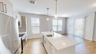 Located at 83 Pleasant Valley St in Methuen, MA, this four-bedroom, two-bathroom residence offers a well-designed single-floor layout with a clean, modern aesthetic throughout. The open-concept kitchen and living area serves as the heart of the home, featuring a large center island with an undermount sink, white shaker-style cabinetry, stainless steel appliances including a refrigerator, range, and microwave, and warm hardwood flooring. Pendant lighting above the island adds a refined touch to the space. The living area extends toward a sliding glass door that opens onto a private balcony, offering scenic outdoor views — an ideal spot for relaxing or entertaining. The four bedrooms are comfortably sized, with the primary bedroom providing a dedicated walk-in closet with built-in shelving. Bedrooms feature neutral carpet, large windows with blinds that allow ample natural light, and soft, neutral wall tones throughout. The two bathrooms are finished with white subway tile surrounds in the tub/shower combinations and chrome fixtures, offering a clean and timeless look. The overall design is bright, neutral, and move-in ready, creating a functional and comfortable living environment.