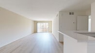 Located at 5633 Colfax Ave in North Hollywood, this one-bedroom, one-bathroom unit offers a well-organized single-floor layout. Light wood-style flooring runs throughout, creating a clean and cohesive aesthetic across all rooms. The open living area is bright and airy, anchored by a ceiling fan and a sliding glass door that leads to a private balcony with views of surrounding palm trees, allowing ample natural light to fill the space. The galley-style kitchen is efficiently designed with white cabinetry, light stone countertops, a peninsula that opens to the living area, and a suite of appliances including a distinctive teal refrigerator, black gas range, and a dishwasher. The bedroom is generously sized, featuring a mirrored sliding closet door and a second sliding glass door with vertical blinds providing additional natural light and outdoor access. The bathroom includes a white vanity with a stone-topped countertop, a large wall mirror, and a combined tub and shower enclosed by frosted sliding glass doors, complemented by wood-style flooring. The unit's neutral warm-toned walls and abundant natural light give the entire space a calm, inviting ambiance throughout.