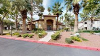 This single-story community presents a striking Spanish-inspired architectural style, characterized by warm stucco exteriors, red tile rooflines, arched entryways, and decorative detailing throughout. The welcoming clubhouse entrance is framed by tall palm trees and carefully maintained desert landscaping, including ornamental shrubs, native ground cover, and seasonal flowering plants, creating an inviting curb appeal.

The centerpiece of the outdoor amenity area is a generously sized freeform swimming pool with crystal-clear turquoise water. A standout feature is the large rock waterfall structure positioned at the heart of the pool, constructed from natural stone and designed to cascade water into the pool below, adding both visual drama and a soothing ambiance. The expansive pool deck surrounds the water on multiple sides, offering ample space for sunbathing and relaxation, complete with lounge chairs positioned to take full advantage of the open sky and abundant sunlight.

Adjacent to the main pool is a separate spa, finished with decorative stone surroundings and equipped with entry handrails. The entire outdoor area is enclosed by fencing and framed by a lush canopy of mature palm trees and evergreens, providing shade and a resort-like atmosphere throughout.