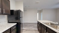 This single-floor residence offers a clean, modern aesthetic with a thoughtfully designed open-concept layout. Light wood-style flooring runs consistently throughout the space, complementing the neutral warm-gray wall tones that create a cohesive and inviting atmosphere.

The kitchen is a functional centerpiece, outfitted with rich dark espresso cabinetry, light granite-style countertops, and black and stainless steel appliances including a refrigerator, range, and microwave. A peninsula with an integrated sink provides additional prep space and connects the kitchen to the adjoining living area. The galley-style configuration maximizes storage and workflow efficiency.

The living area is bright and open, featuring sliding glass doors that invite natural light and provide outdoor access. Ceiling fans add to the comfort of both the living and bedroom spaces.

The bedrooms are well-sized, each featuring wood-style flooring, windows with natural light, and access to closet storage. One bedroom includes a sliding double-door closet and direct access to a private bathroom. The bathrooms are finished with dark vanity cabinetry, granite-style countertops, a large mirror, and a walk-in shower with clean white surround. A secondary bathroom features similar finishes with a standalone shower and wood-look tile flooring, maintaining design consistency throughout the home.