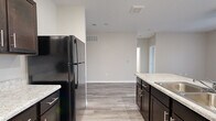 This single-floor residence offers a clean, modern aesthetic with a thoughtfully designed open-concept layout. Light wood-style flooring runs consistently throughout the space, complementing the neutral warm-gray wall tones that create a cohesive and inviting atmosphere.

The kitchen is a functional centerpiece, outfitted with rich dark espresso cabinetry, light granite-style countertops, and black and stainless steel appliances including a refrigerator, range, and microwave. A peninsula with an integrated sink provides additional prep space and connects the kitchen to the adjoining living area. The galley-style configuration maximizes storage and workflow efficiency.

The living area is bright and open, featuring sliding glass doors that invite natural light and provide outdoor access. Ceiling fans add to the comfort of both the living and bedroom spaces.

The bedrooms are well-sized, each featuring wood-style flooring, windows with natural light, and access to closet storage. One bedroom includes a sliding double-door closet and direct access to a private bathroom. The bathrooms are finished with dark vanity cabinetry, granite-style countertops, a large mirror, and a walk-in shower with clean white surround. A secondary bathroom features similar finishes with a standalone shower and wood-look tile flooring, maintaining design consistency throughout the home.