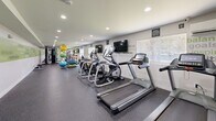 Located at 7669 Marcin Dr in Glen Burnie, MD, this well-equipped fitness center offers a comprehensive exercise environment across a single, open floor. The room is designed with functionality and motivation in mind, featuring durable speckled rubber flooring that provides both safety and comfort during workouts.

The cardio section is prominently lined with multiple treadmills, elliptical trainers, and a stationary bike, each equipped with individual digital displays for tracking workout metrics. Wall-mounted flat-screen televisions are positioned for easy viewing during cardio sessions. On the opposite end, a multi-function cable strength machine, weight bench, and an assortment of stability balls and medicine balls on a dedicated rack cater to strength and functional training needs.

Natural light filters in through slatted blinds on multiple windows, complemented by recessed ceiling lighting that ensures the space remains bright throughout the day. A water dispenser station is conveniently located along the wall for easy hydration access.

A standout design element is the motivational typography wall graphics — featuring words such as "limitless," "determination," "focus," and "strength" — displayed in green and gray tones across multiple walls, reinforcing an energizing atmosphere. A wall-mounted mirror on one end further enhances the sense of openness. The overall ambiance is clean, modern, and purpose-built for an effective fitness experience.