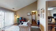 This updated 2-bedroom, 2-bathroom single-story residence offers a well-designed layout that balances comfort and functionality. The living room serves as the heart of the home, featuring striking vaulted ceilings that amplify the sense of space and a sliding glass door that fills the room with natural light while providing outdoor access. Dark hardwood-style flooring runs throughout the main living areas, adding warmth and visual continuity.

The kitchen is well-equipped with stainless steel appliances, including a range, microwave, dishwasher, and refrigerator, complemented by light-toned cabinetry and dark countertops. A dedicated dining area sits adjacent, providing a defined space for meals. The hallway connects the living spaces to both bedrooms, each finished with plush carpet flooring. The primary bedroom features a ceiling fan, natural light from windows with blinds, and ample room for furnishings. The second bedroom offers similar comfort and versatility. Neutral taupe-toned walls throughout create a cohesive, calming ambiance, while textured ceilings add a traditional architectural detail present across all rooms.