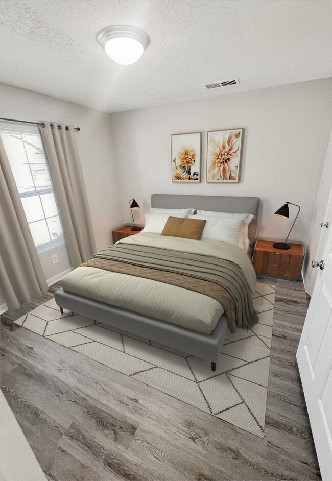 Bedroom with upholstered bed, nightstands, table lamps, decorative wall art, area rug, and wood look plank flooring - Pendleton Townhomes
