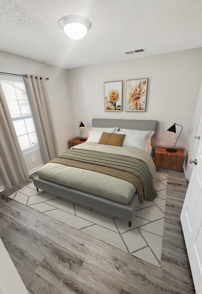 Dormitorio con cama tapizada, mesitas de noche, lámparas de mesa, arte de pared decorativo, alfombra y piso de tablones con apariencia de madera. - Pendleton Townhomes