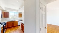 This single-floor residence offers a thoughtfully designed layout that balances comfort and functionality. The kitchen is a standout feature, showcasing warm honey-toned wood cabinetry, light countertops, a marble-style tile backsplash, and a full suite of stainless steel appliances including a gas range, microwave, refrigerator, and dishwasher. A large window above the sink fills the space with natural light and offers outdoor views. A kitchen island provides additional prep and dining space, with pendant lighting overhead adding a modern touch. Hardwood-style flooring flows seamlessly through the main living areas, including a generously sized living room equipped with a ceiling fan and multiple windows that invite abundant natural light. The bedroom features neutral carpet and crisp white walls, offering a calm and restful environment. The bathroom is well-appointed with large-format marble-look tile lining the tub-shower surround, hexagonal floor tiles, and clean white fixtures. A dedicated laundry room with side-by-side washer and dryer units and a wire storage shelf above adds everyday convenience. Throughout the home, six-panel interior doors and a neutral color palette create a cohesive, clean aesthetic.