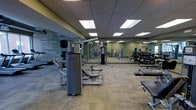 This fitness center is designed to support a wide range of workout routines in a clean, professional environment. The space is laid out across a single floor and features a generous open layout that accommodates multiple exercise zones without feeling cramped. Overhead, a suspended ceiling with recessed panel lighting provides bright, even illumination throughout the room. The flooring consists of durable, low-pile carpet suited for gym use.

The strength training area is the centerpiece of the facility, outfitted with a variety of cable and resistance machines from Paramount, along with adjustable benches and functional training stations. A dedicated free weight section lines one side of the room, featuring a full rack of dumbbells arranged in ascending order for easy access. Full-length mirrors along the walls expand the sense of space and allow users to monitor their form during exercise.

An accent wall displaying motivational words and phrases in a bold typographic mural adds character and energy to the environment. The overall ambiance is focused and functional, with a neutral color palette of grays and greens that contributes to a calm yet motivating atmosphere. The facility is well-organized and thoughtfully arranged to ensure ease of movement between equipment stations.