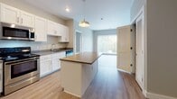 This single-story residence at 430 Warren St in Dayton, Ohio offers a well-designed, open-concept layout with consistent light wood-style flooring running throughout the main living areas. The kitchen serves as a central focal point, featuring white shaker-style cabinetry with brushed nickel hardware, dark countertops, and a full suite of stainless steel appliances including a gas range, built-in microwave, dishwasher, and refrigerator. A center island with a light-toned countertop provides additional workspace and casual seating potential, while a pendant light overhead adds a finishing touch. The kitchen flows naturally into the living area, which benefits from a sliding glass door fitted with vertical blinds, allowing ample natural light and outdoor access.

The bedrooms are carpeted for comfort, each equipped with a ceiling fan and vertical-blind-covered windows that bring in natural light. The bathrooms feature wood-style flooring, white vanities with mirrors and wall-mounted lighting, a full soaking tub with shower, and accessibility grab bars. Louvered closet doors and neutral wall tones contribute to the clean, practical aesthetic found throughout the space.