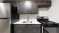 This single-floor residence offers a clean, updated aesthetic with a cohesive design language carried throughout its rooms. The kitchen stands out as a highlight, showcasing dark charcoal shaker-style cabinetry paired with crisp white quartz countertops and a classic white subway tile backsplash. A stainless steel undermount sink and a stainless steel gas range complete the functional and stylish cooking space, while ample upper and lower cabinetry provides generous storage.

The living and bedroom areas share a consistent look, featuring light grey laminate hardwood flooring that adds warmth and easy maintenance. Neutral grey walls and white trim create a calm, versatile backdrop, and each room benefits from natural light through blinded windows. Baseboard radiators are present throughout, providing efficient heating. The layout flows naturally between rooms, with open doorways connecting the living space to the rest of the unit.

The bathroom is a standout feature, dressed in large-format marble-look porcelain tiles from floor to tub surround, lending a luxurious feel. A white soaking tub, chrome fixtures, a pedestal-style vanity with brushed nickel hardware, and a mirrored medicine cabinet round out the space. Together, the finishes across this residence reflect a well-executed, modern renovation.