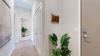 This 2-bedroom, 2-bathroom residence is designed with a modern, open-concept layout that maximizes both functionality and comfort. The combined kitchen and living area serves as the heart of the home, featuring light hardwood flooring, recessed and pendant lighting, and large sliding glass doors that flood the space with natural light and provide access to an outdoor area with views of the surrounding neighborhood. The kitchen is outfitted with white shaker cabinetry, stainless steel appliances, a central island with a white quartz countertop and bar seating, making it equally suited for cooking and entertaining. The primary bedroom offers a calm, neutral palette with plush carpet flooring and direct access to a dedicated walk-in closet and a private en-suite bathroom. The en-suite features a long dual-sink vanity with white cabinetry and matte black hardware, warm wood-tone flooring, and tasteful decorative wall art. The second bedroom is similarly well-proportioned, with its own closet access and proximity to the second full bathroom. A clean, well-lit hallway connects the living spaces to the bedrooms, accented by crisp white doors and subtle decorative touches. Throughout, the residence maintains a cohesive, contemporary aesthetic with neutral tones and quality finishes.