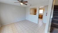 This two-story home offers a practical and straightforward layout across both levels. The main living area on the ground floor is finished with large-format light tile flooring and features a ceiling fan overhead. A pass-through opening connects the living space directly to the kitchen, providing an open sightline between the two areas. An adjacent dining space mirrors this tile flooring and also benefits from the pass-through window, allowing natural light to filter through from the kitchen's exterior window.

The kitchen is well-appointed with warm-toned wooden cabinetry that extends both above and below the countertops, offering generous storage. A double-basin stainless steel sink sits beneath a window fitted with blinds, allowing natural light in. A white electric range and refrigerator complete the appliance suite.

Upstairs, the living spaces transition to plush carpeted flooring. A spacious room features a ceiling fan and a textured ceiling, along with a built-in half-wall nook. The upper level also includes a generously sized walk-in closet outfitted with dual hanging rods and a tall central shelving unit, providing ample organization options. The bathroom is clean and functional, featuring a full soaking tub with a shower and chrome fixtures throughout.