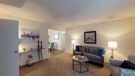 Located at Devonshire Gardens, this single-floor residence offers a well-designed layout that balances comfort and functionality. The living room serves as the heart of the home, featuring plush wall-to-wall carpeting and a neutral color palette of soft whites and warm beiges that create a calm, welcoming atmosphere. The space is generously proportioned, providing ample room for seating and relaxation. An open passageway connects the living room to the adjacent dining area, promoting an easy flow between the two spaces and enhancing the sense of openness throughout. The dining area benefits from natural light filtering in through a window, brightening the interior and adding an airy quality to the space. Smooth, textured ceilings and clean white walls throughout provide a versatile backdrop that complements a variety of interior styles. The transition between the living and dining areas is seamless, making the layout ideal for both everyday living and entertaining. Overall, the residence at Devonshire Gardens presents a practical and comfortable living environment with a cohesive, understated aesthetic.
