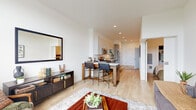 This thoughtfully designed single-floor residence combines modern aesthetics with functional living in a clean, contemporary style. Light hardwood flooring flows throughout, complementing the crisp white walls and creating a warm, cohesive atmosphere.

The open-concept living and dining area is anchored by large windows that frame outdoor views and flood the space with natural light. The layout connects seamlessly to a well-designed kitchen, which features two-tone cabinetry — white upper cabinets paired with warm wood-grain lower cabinets — stone countertops, a white subway tile backsplash, and a full suite of stainless steel appliances including a gas range, microwave, and dishwasher. A breakfast bar with seating bridges the kitchen and living area, making it ideal for casual dining and entertaining.

A private hallway connects the living areas to the bedroom and bathroom, offering a sense of separation and quiet. The bathroom is finished with clean, minimal detailing, including a wood-grain vanity with white countertop, a glass-enclosed walk-in shower, and tile flooring. In-unit laundry is also available, adding everyday convenience.

Throughout the space, the design emphasizes simplicity, natural materials, and an abundance of light — resulting in a calm, inviting environment suited for modern living.