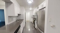 Located at 295 Dufferin St in Toronto's vibrant Dufferin Grove neighbourhood, this 2-bedroom, 1-bathroom unit offers a well-designed, functional layout across a single floor. The open-concept living area is finished with warm hardwood-style flooring and crisp white walls, creating a bright and welcoming atmosphere. A large window at the end of the living room invites natural light and frames pleasant green outdoor views, enhancing the sense of openness.

The galley-style kitchen is thoughtfully appointed with white shaker cabinetry, grey tile backsplash, dark countertops, polished tile flooring, and a full suite of stainless steel appliances including a refrigerator, stove, and over-the-range microwave. Both bedrooms feature the same hardwood-style flooring and windows overlooking lush greenery, offering a calm and private feel. The primary bedroom provides a comfortable amount of space, while the second bedroom is well-suited as a guest room or home office.

The bathroom is finished with classic white subway tile surrounding a full soaker tub and shower combination, complemented by a wall-mounted mirror and clean white fixtures. A hallway connects the main areas efficiently, and the layout makes excellent use of the available space. This unit combines modern finishes with a practical design in a well-located Toronto address.