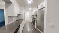Located at 295 Dufferin St in Toronto's vibrant Dufferin Grove neighbourhood, this 2-bedroom, 1-bathroom unit offers a well-designed, functional layout across a single floor. The open-concept living area is finished with warm hardwood-style flooring and crisp white walls, creating a bright and welcoming atmosphere. A large window at the end of the living room invites natural light and frames pleasant green outdoor views, enhancing the sense of openness.

The galley-style kitchen is thoughtfully appointed with white shaker cabinetry, grey tile backsplash, dark countertops, polished tile flooring, and a full suite of stainless steel appliances including a refrigerator, stove, and over-the-range microwave. Both bedrooms feature the same hardwood-style flooring and windows overlooking lush greenery, offering a calm and private feel. The primary bedroom provides a comfortable amount of space, while the second bedroom is well-suited as a guest room or home office.

The bathroom is finished with classic white subway tile surrounding a full soaker tub and shower combination, complemented by a wall-mounted mirror and clean white fixtures. A hallway connects the main areas efficiently, and the layout makes excellent use of the available space. This unit combines modern finishes with a practical design in a well-located Toronto address.