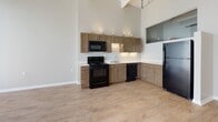 Located at 22 S Saint Clair St in downtown Dayton, Ohio, this single-floor unit offers a thoughtfully designed layout with a blend of industrial and contemporary elements. The space is defined by expansive floor-to-ceiling windows that flood the interior with abundant natural light, casting distinctive patterns across the light wood-look flooring throughout. Exposed ductwork running along the ceiling adds an industrial character that complements the otherwise clean, neutral aesthetic.

The open main area provides generous room for flexible use, benefiting greatly from the striking window wall that frames views of the surrounding urban environment. The kitchen is well-appointed with warm-toned cabinetry, white countertops, and a full suite of black appliances including a refrigerator, range, microwave, and dishwasher. Tall ceilings in the kitchen area enhance the sense of openness, with upper cabinets extending toward the ceiling for ample storage. A glass partition detail adds a modern architectural touch.

The unit includes two bathrooms: one featuring a walk-in shower with a single-sink vanity, and another with a full soaking tub/shower combination, also paired with a single-sink vanity. Both bathrooms feature wood-look flooring, dark wood cabinetry, and brushed nickel fixtures, maintaining a consistent and cohesive design throughout the space.