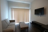 This single-floor unit is designed with a clean, contemporary aesthetic that emphasizes functionality and modern style. The entryway corridor sets the tone with rich wood-look flooring, dark door trim accents, and charcoal-toned interior doors that carry through the space consistently. A smart thermostat panel is conveniently located near the entry, alongside access to multiple rooms and a front door with a frosted glass panel that allows diffused natural light into the hallway.

The kitchen is outfitted with dark espresso cabinetry contrasted by crisp white countertops and a classic tile backsplash. Black appliances — including an electric range, over-the-range microwave, and dishwasher — provide a cohesive, modern look, while the stainless steel sink adds a practical touch.

The living area is bright and welcoming, featuring a window with vertical blinds and access to an outdoor balcony, allowing natural light to fill the room and offering views of the surrounding exterior. The space is open enough to accommodate comfortable seating arrangements.

A bedroom area features hardwood-style flooring and direct access to a bathroom, providing a convenient and private layout. Throughout the unit, the hallways are thoughtfully designed with accessibility features, including a grab bar, reflecting an inclusive approach to the space's design. Overall, the unit combines practicality with a modern edge.