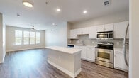 This thoughtfully designed 1-bedroom, 1-bathroom unit offers a efficient and modern living experience across a single floor. The open-concept layout seamlessly connects the kitchen and living room, creating a bright and functional shared space. The kitchen is a standout feature, equipped with stainless steel appliances including a range, built-in microwave, dishwasher, and refrigerator. White shaker-style cabinetry pairs with a grey subway tile backsplash and a large central island with a quartz countertop, providing ample prep space and additional seating. Wood-style plank flooring runs throughout the unit, adding warmth and cohesion to the design. The living area benefits from natural light provided by a window and includes a ceiling fan overhead. The spacious bedroom features its own ceiling fan, large windows with blinds offering outdoor views, and direct access to a closet and hallway. The bathroom is clean and modern, featuring a white subway tile tub-surround, a white vanity with quartz countertops, and wood-look tile flooring. A dedicated closet provides additional storage. Neutral wall tones and recessed lighting throughout contribute to the unit's bright, contemporary ambiance.