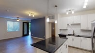 This well-appointed single-floor residence offers a thoughtfully designed open-concept layout that seamlessly connects the kitchen, dining, and living areas. The kitchen serves as the centerpiece, showcasing sleek white cabinetry, dark granite countertops, a classic white subway tile backsplash, and a full suite of stainless steel appliances including a french door refrigerator, electric range with microwave, and dishwasher. A large kitchen island with a matching granite surface provides additional prep space and casual seating. Pendant lighting and track lighting illuminate the kitchen and living areas, enhancing the modern aesthetic throughout.

The living room features durable wood-look flooring and a bold navy blue accent wall that adds a striking design element, along with access to an outdoor area through a glass-panel door. Natural light filters in through window treatments.

The bedrooms are finished with plush carpeting and offer generous closet space, including a walk-in closet in the primary bedroom. The bathrooms are finished with wood-look tile flooring, white vanity cabinetry, dark countertops, and a tiled shower-tub combination. A utility area with an in-unit washer and dryer is also present, adding everyday convenience to this well-designed residence.