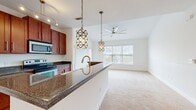 Located at 4200 Academy Dr in Opelika, Alabama, this single-floor residence offers three bedrooms, two bathrooms, and a well-organized layout across a comfortable footprint. The open-concept kitchen and living area serves as the heart of the home, where rich cherry-toned cabinetry pairs with dark granite-style countertops and terracotta tile flooring. A large kitchen island with a built-in sink anchors the space, while two geometric pendant lights add a stylish focal point. Stainless steel appliances, including a microwave and refrigerator, complement the kitchen's functional design. The adjacent living area transitions seamlessly from tile to plush carpeting, with a ceiling fan overhead and a wide window allowing ample natural light and outdoor views. The three bedrooms are carpeted and bright, each featuring ceiling fans and windows with exterior views. The primary bedroom offers a comfortable, well-proportioned layout. Both bathrooms are finished with terracotta tile flooring, dark-countered vanities with cherry cabinetry, and tub-shower combinations with white tile surrounds. A hallway connects the private areas of the home, which also includes two closets for additional storage.