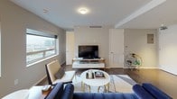 This thoughtfully designed 1-bedroom, 1.5-bathroom model unit showcases a contemporary aesthetic with high-quality finishes throughout. The open-concept living area features rich hardwood flooring, neutral tones, and large windows that frame sweeping urban skyline views, filling the space with natural light. The living room accommodates a comfortable seating arrangement centered around a round coffee table with gold accents, complementing the modern furnishings.

The adjacent dining area is anchored by a marble-top round table beneath a sculptural globe chandelier, creating an elegant yet approachable atmosphere. The kitchen is outfitted with dark espresso cabinetry, white quartz countertops, stainless steel appliances including a French door refrigerator, electric range, microwave, and dishwasher, all set against a clean tile backsplash with recessed lighting above.

The bedroom is a serene retreat with a ceiling fan, hardwood flooring, and a window offering city views. The full bathroom features a glass-enclosed walk-in rain shower, a sleek double vanity with under-mount sink, and light stone-look tile flooring. A separate half bathroom offers large-format grey tile walls and refined fixtures, providing added convenience for guests.