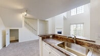 Located at 100 Town Walk Dr in Hamden, CT, this residence offers a thoughtfully designed layout that balances comfort and functionality. The living room serves as the centerpiece of the home, boasting dramatic vaulted ceilings that rise to impressive heights, a classic fireplace with a clean white mantle, and large windows — including a striking upper transom window — that flood the space with natural light. Plush carpeting throughout adds warmth underfoot.

The kitchen is open and efficient, featuring white cabinetry, dark granite-style countertops, stainless steel appliances including a gas range and refrigerator, and a peninsula with a double sink that connects seamlessly to the living area. Wood-look flooring runs through the kitchen, providing a practical and attractive finish.

The bedrooms are generously sized, each carpeted and filled with natural light from well-placed windows. Multiple bedrooms include spacious walk-in closets outfitted with wire shelving systems, offering abundant storage. A full bathroom serves the home with a tiled tub/shower combination, a white vanity with under-cabinet storage, and wood-look flooring. A staircase visible from the main living area adds architectural interest to the overall design.