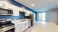 Located at 818 Fourth St NW in Faribault, Minnesota, this thoughtfully designed one-bedroom, one-bathroom unit offers a efficient and modern living experience across a single floor. The open-concept kitchen serves as a centerpiece, featuring white shaker-style cabinetry with matte black hardware, light quartz countertops, and a bold navy blue accent wall that adds a striking visual element. Stainless steel appliances — including a range, over-the-range microwave, and dishwasher — complement the space, while a large kitchen island with a matching quartz surface provides additional prep and seating space. Light wood-tone flooring flows throughout the main living areas, lending warmth and continuity. The bedroom is generously proportioned, finished with plush carpeting and a large window that invites natural light and outdoor views of the surrounding neighborhood. Clean white panel doors and soft neutral wall tones keep the space feeling bright and airy. A dedicated closet features built-in wire shelving for organized storage. The bathroom offers a long vanity with white cabinetry, quartz countertop, and an undermount sink, with light wood flooring extending through the hallway that connects back to the main living area. The overall aesthetic is clean, contemporary, and move-in ready.
