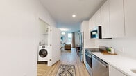 Located at 35 E Pleasant St in Amherst, MA, this thoughtfully designed one-bedroom, one-bathroom unit offers a compact yet highly functional layout across a single floor. Light wood-tone flooring runs throughout, complementing the clean white walls and modern finishes that define the space.

The galley-style kitchen is equipped with stainless steel appliances, including a full-size refrigerator, range with oven, built-in microwave, and dishwasher. Sleek white cabinetry extends to the ceiling, maximizing storage, while white countertops and an undermount sink complete the contemporary look. A dedicated in-unit washer is conveniently tucked into a closet just off the entryway. The front door features a keypad entry system for added security.

The generously sized primary bedroom serves as the central living area, combining sleeping, living, and dining functions in an open arrangement. A large window floods the room with natural light and offers outdoor views, while a wall-mounted mini-split system provides climate control. The bedroom also includes a spacious closet with built-in shelving.

The bathroom is clean and minimalist, finished with the same light wood flooring and bright white walls, featuring a shower with a curtain enclosure. Overall, the unit presents a modern, efficient living environment well-suited for its location near the University of Massachusetts Amherst campus.